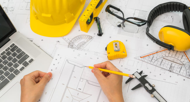 Hand over Construction plans with yellow helmet and drawing tool Hand over Construction plans with yellow helmet and drawing tools on blueprints